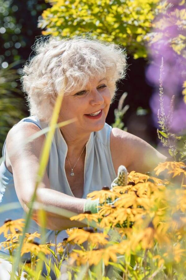 Una donna anziana sistema i fiori nel suo giardino.