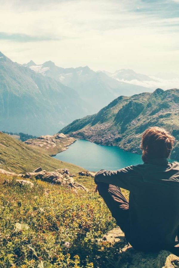 Un viaggiatore sta meditando rilassandosi su una roccia mentre ammira una magnifica veduta delle montagne e del lago.
