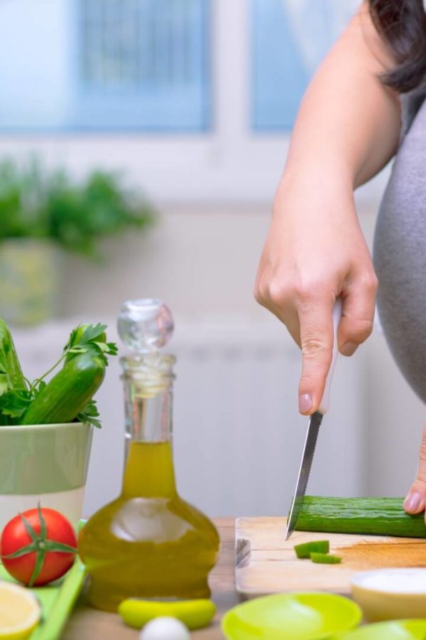 Беременная женщина нарезает овощи для здорового обеда.