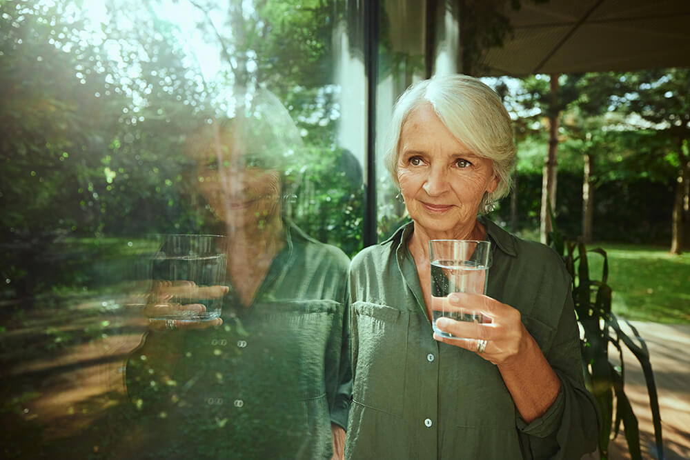 A woman who is drinking a glass of water, which is good for efficient digestion.